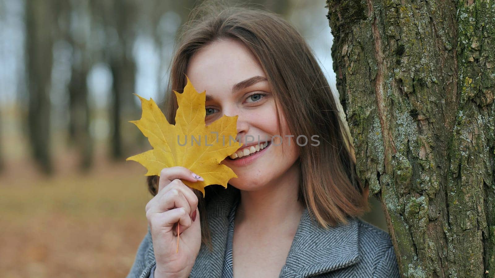 Beautiful happy woman with a smile holds an autumn yellow leaf near the face