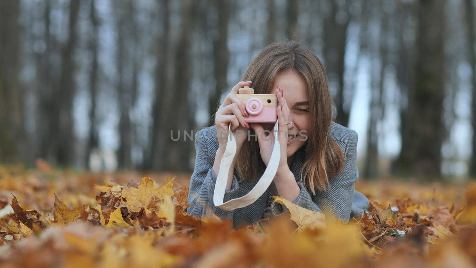A young beautiful girl takes pictures in an autumn park using a toy camera