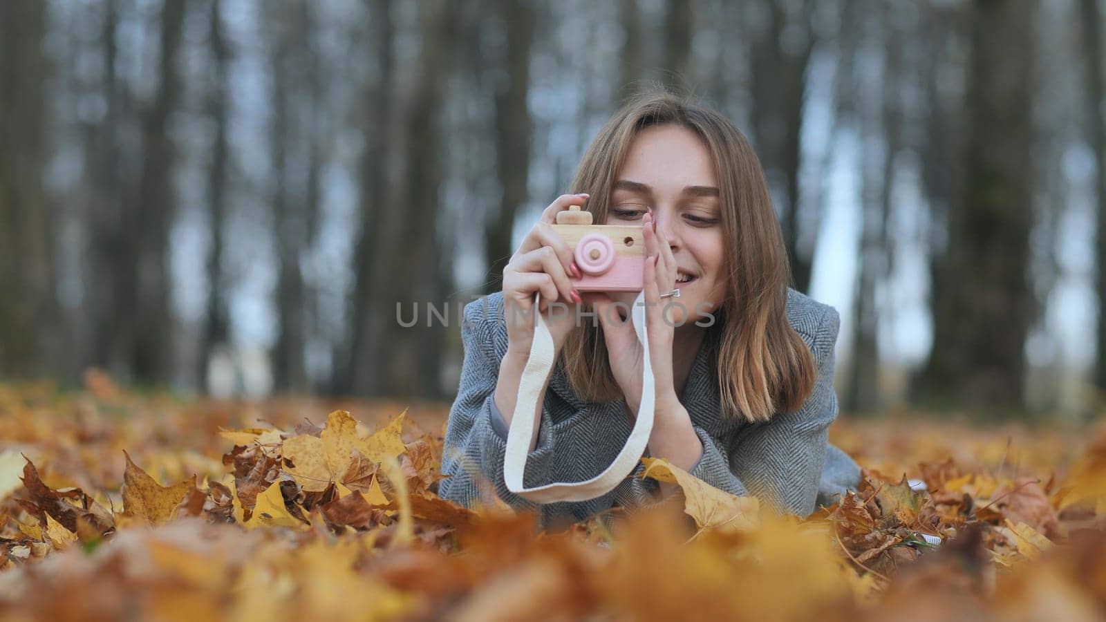 A young beautiful girl takes pictures in an autumn park using a toy camera