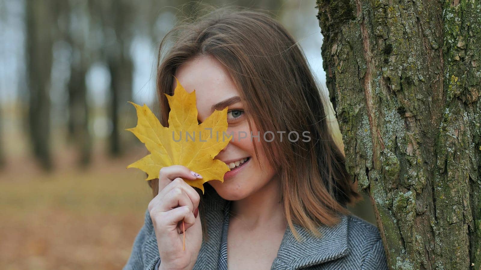 Beautiful happy young girl with a smile holds an autumn yellow leaf near the face