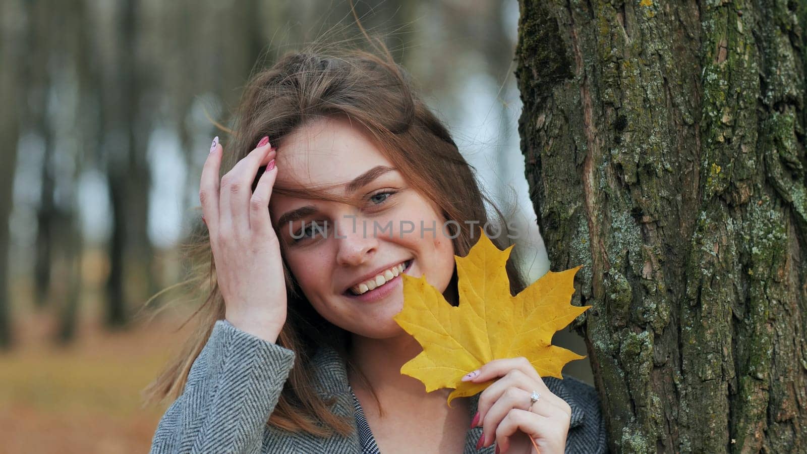 Beautiful happy woman with a smile holds an autumn yellow leaf near the face
