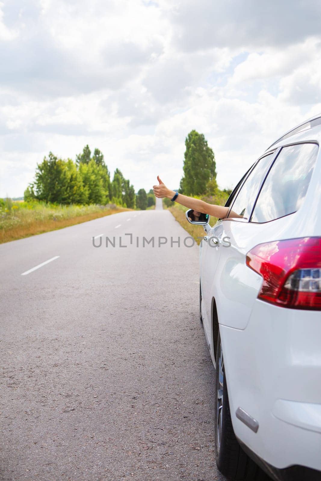 A young girl driving a car, pulls her hand out of the window and shows like