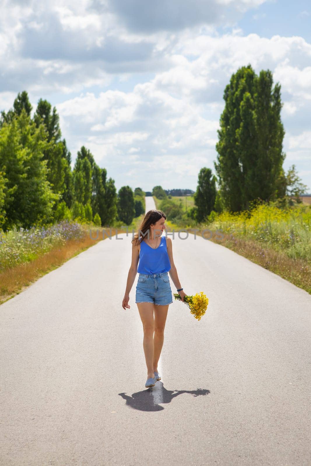 Attractive girl, posing, walking with a bouquet of yellow flowers in the middle of the asphalt road near the field, copy space for content