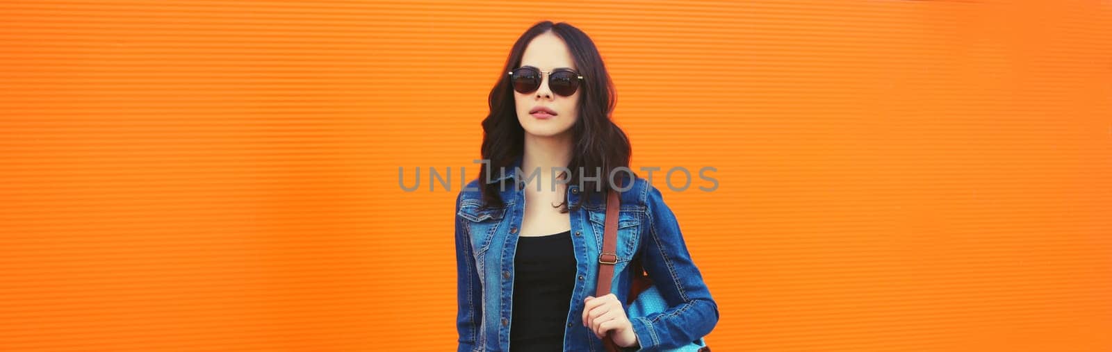 Portrait of beautiful brunette young woman in sunglasses posing in the city on orange background, copy space