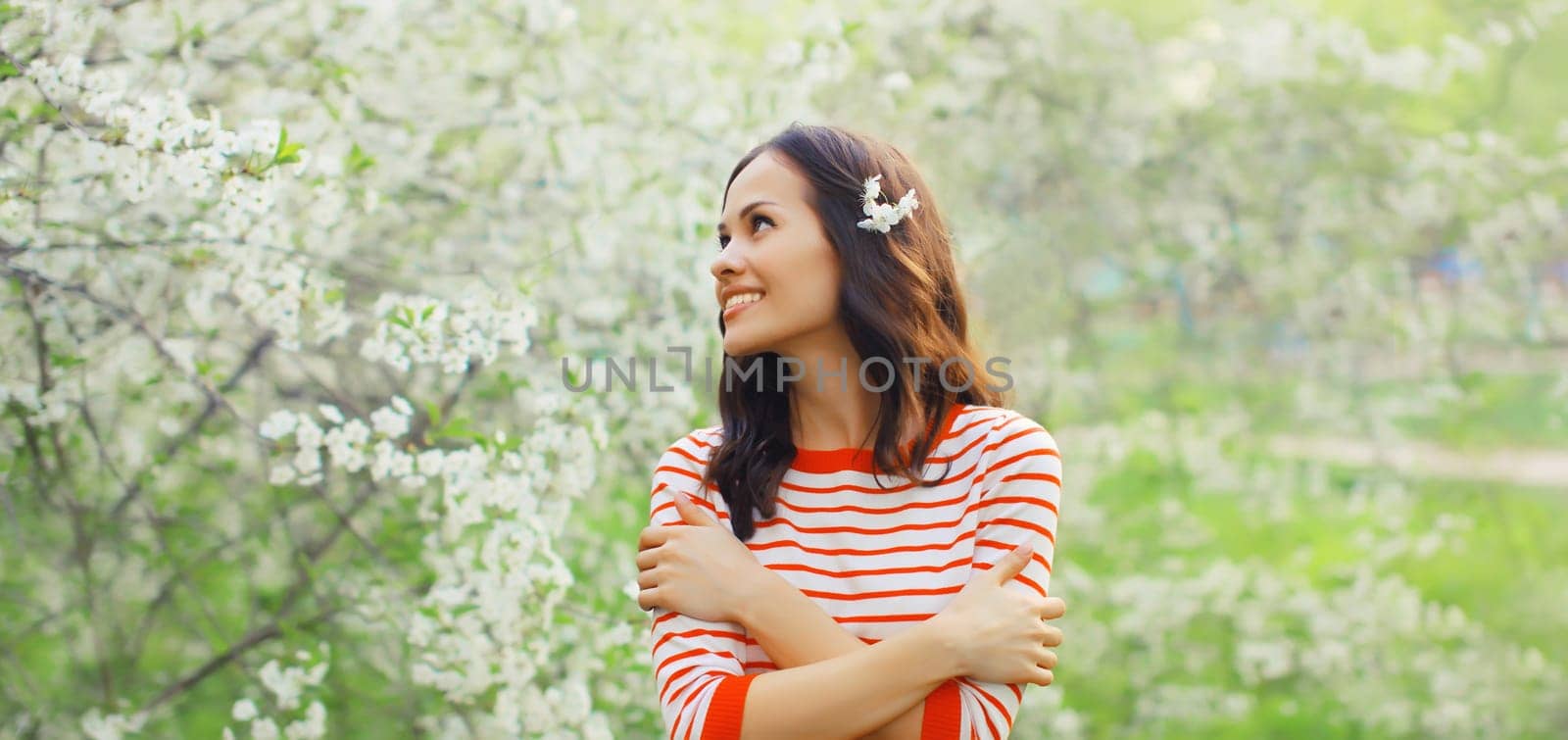 Portrait of lovely happy smiling young woman in spring blooming garden with white flowers on the trees in park