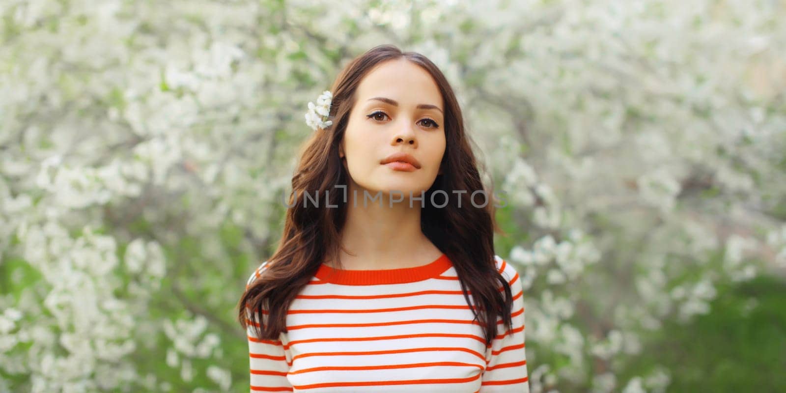 Portrait of lovely young woman in spring blooming garden with white flowers on the trees in park