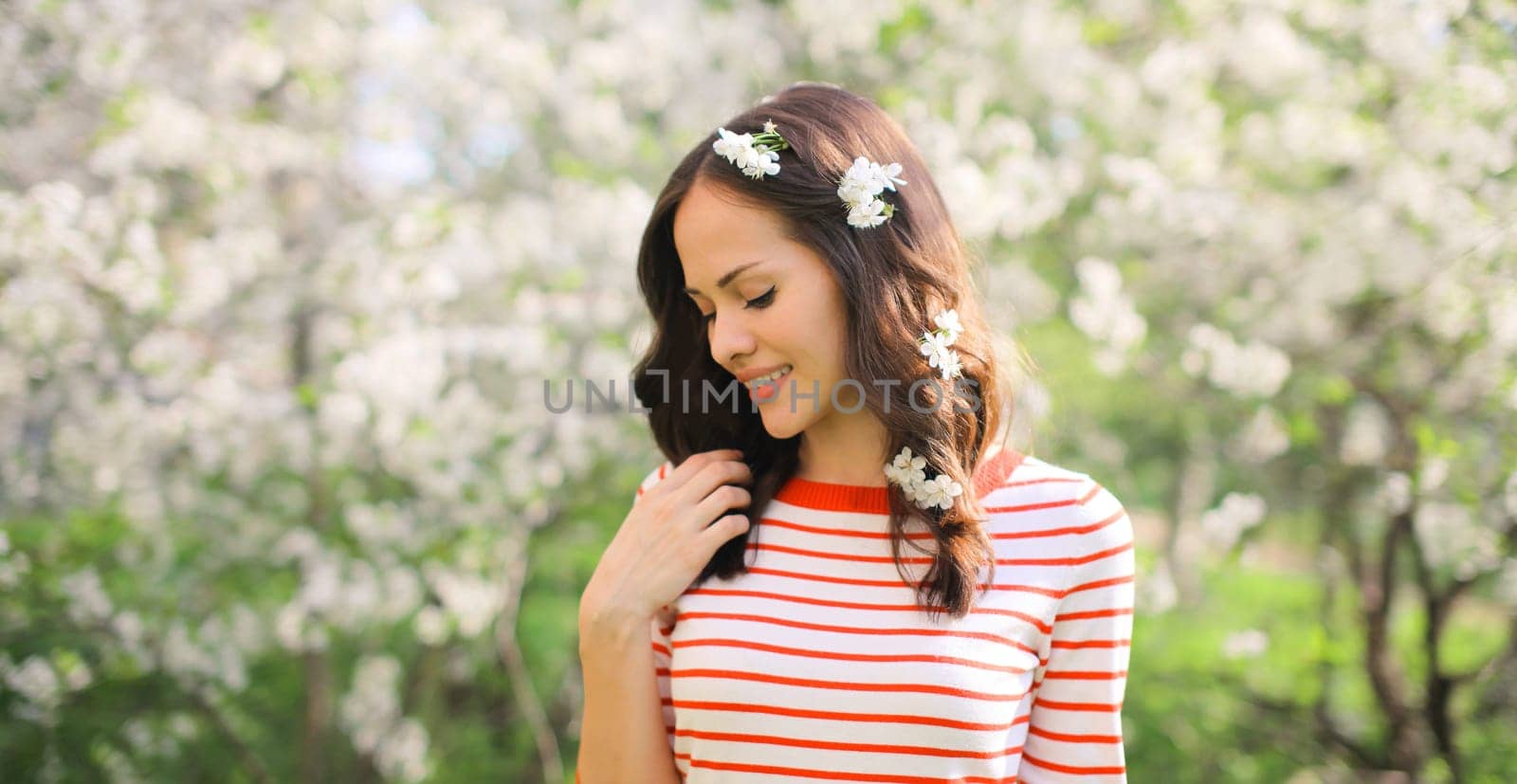 Portrait of lovely happy smiling young woman in spring blooming garden with white flowers on the trees in park