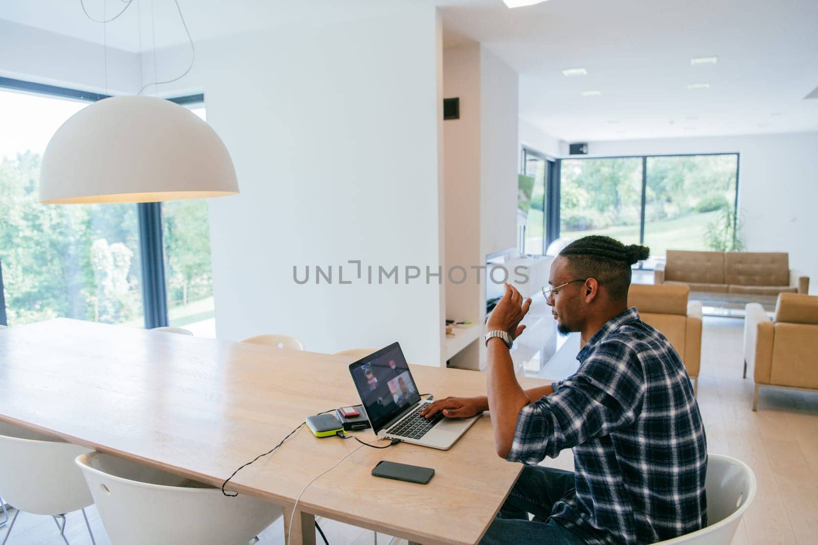 African American influencer in glasses sitting at a table in a modern living room, using a laptop for business video chat, conversation with friends and entertainment