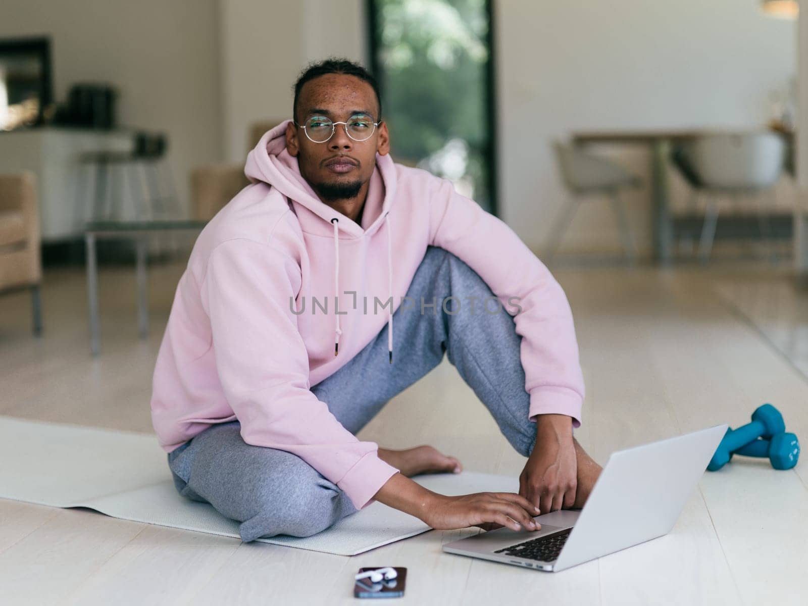 African American man in glasses sitting at a table in a modern living room, using a laptop for business video chat, conversation with friends and entertainment