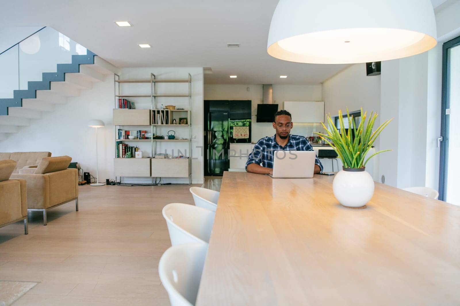 African American influencer in glasses sitting at a table in a modern living room, using a laptop for business video chat, conversation with friends and entertainment