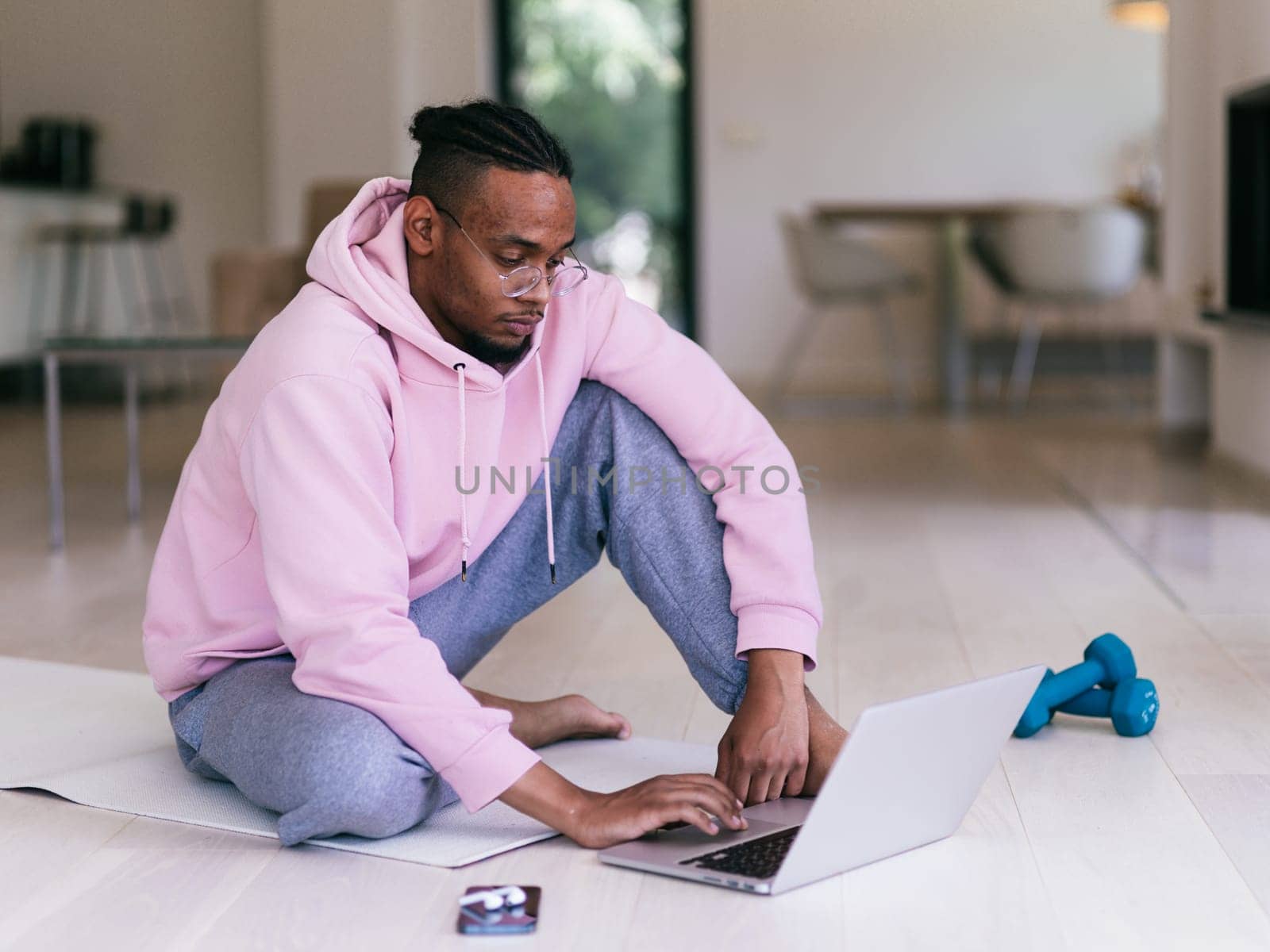 African American man in glasses sitting at a table in a modern living room, using a laptop for business video chat, conversation with friends and entertainment