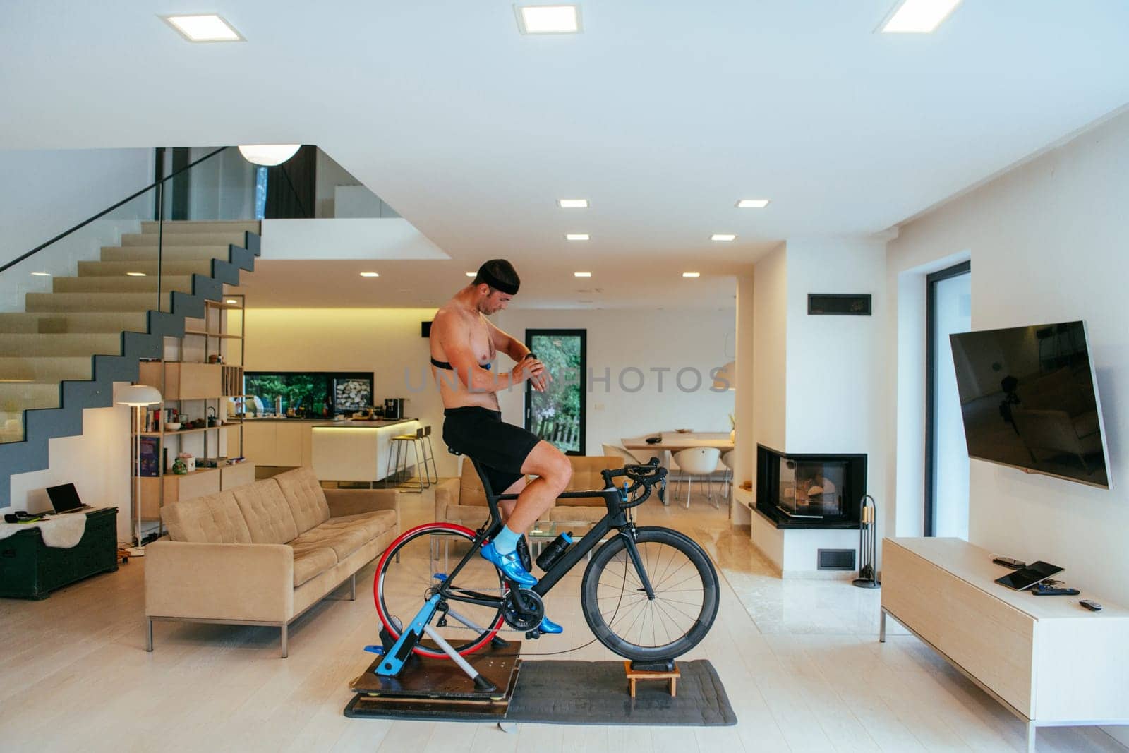 A triathlete riding a triathlon bike on a machine simulation in a modern living room.