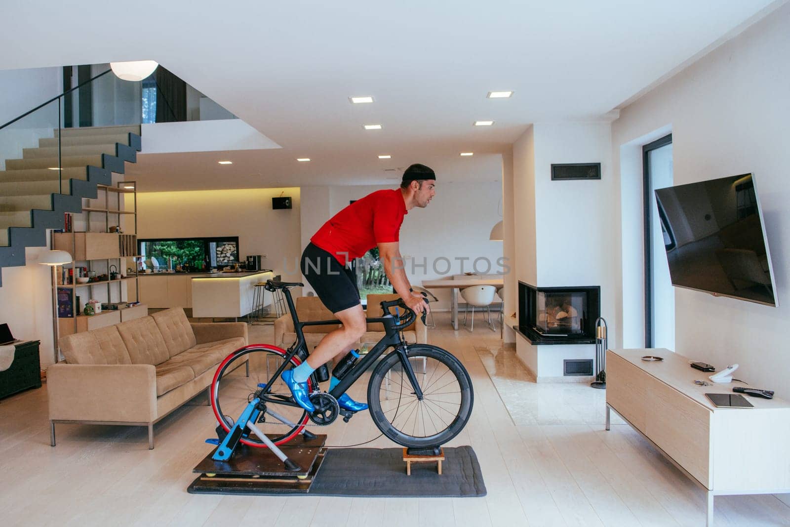 A triathlete riding a triathlon bike on a machine simulation in a modern living room.