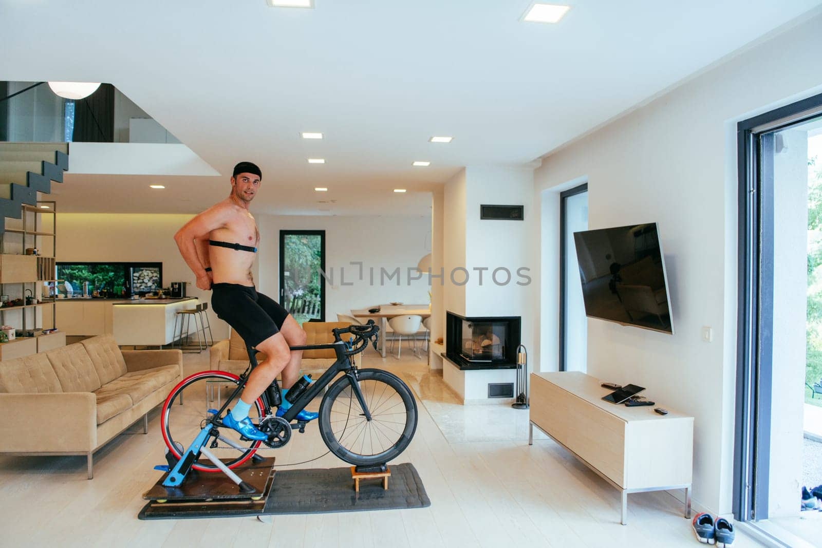 A triathlete riding a triathlon bike on a machine simulation in a modern living room.