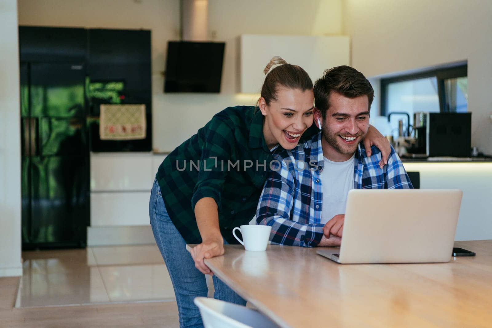 A young married couple is talking to parents, family and friends on a video call via a laptop while sitting in the living room of their modern house