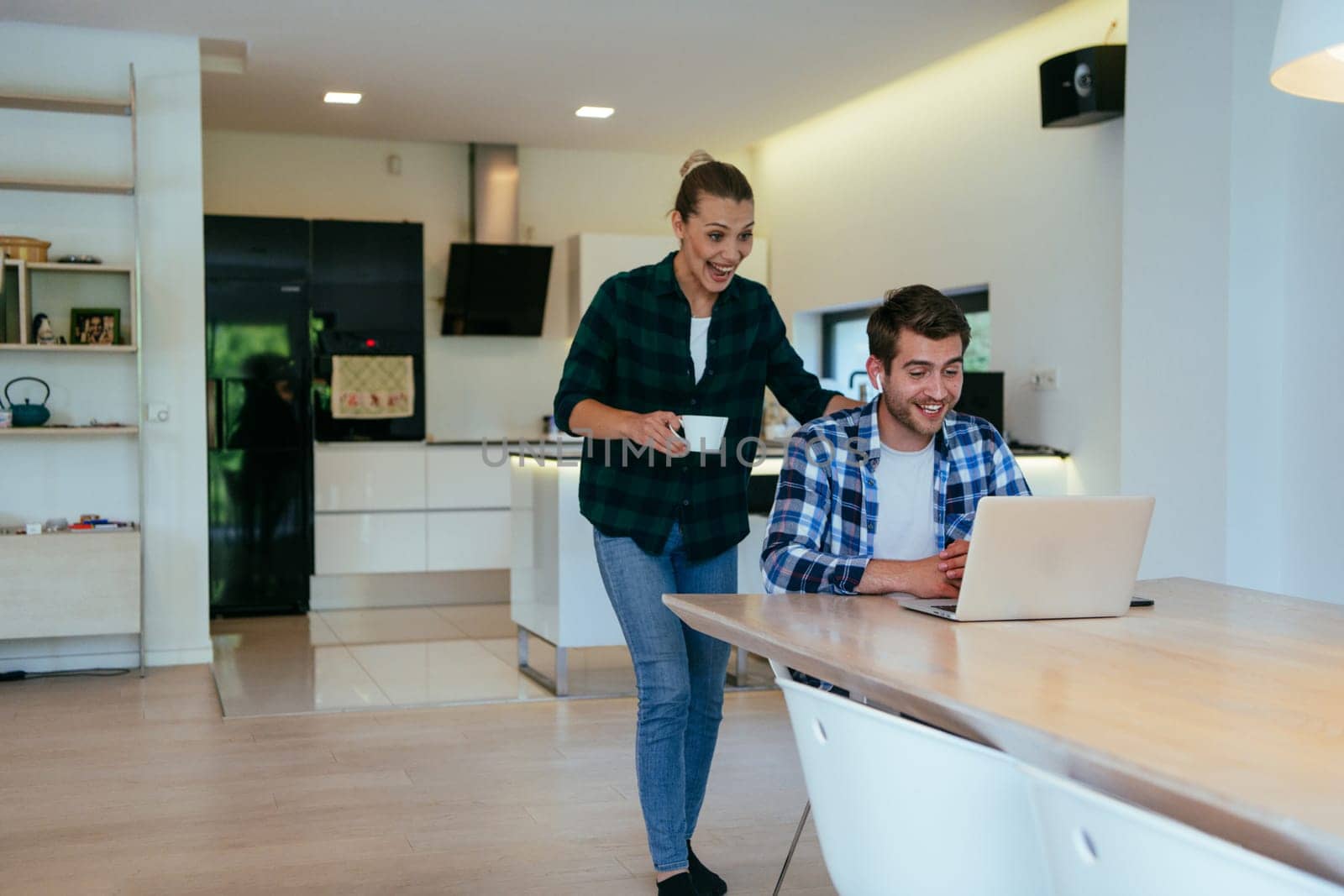 A young married couple is talking to parents, family and friends on a video call via a laptop while sitting in the living room of their modern house