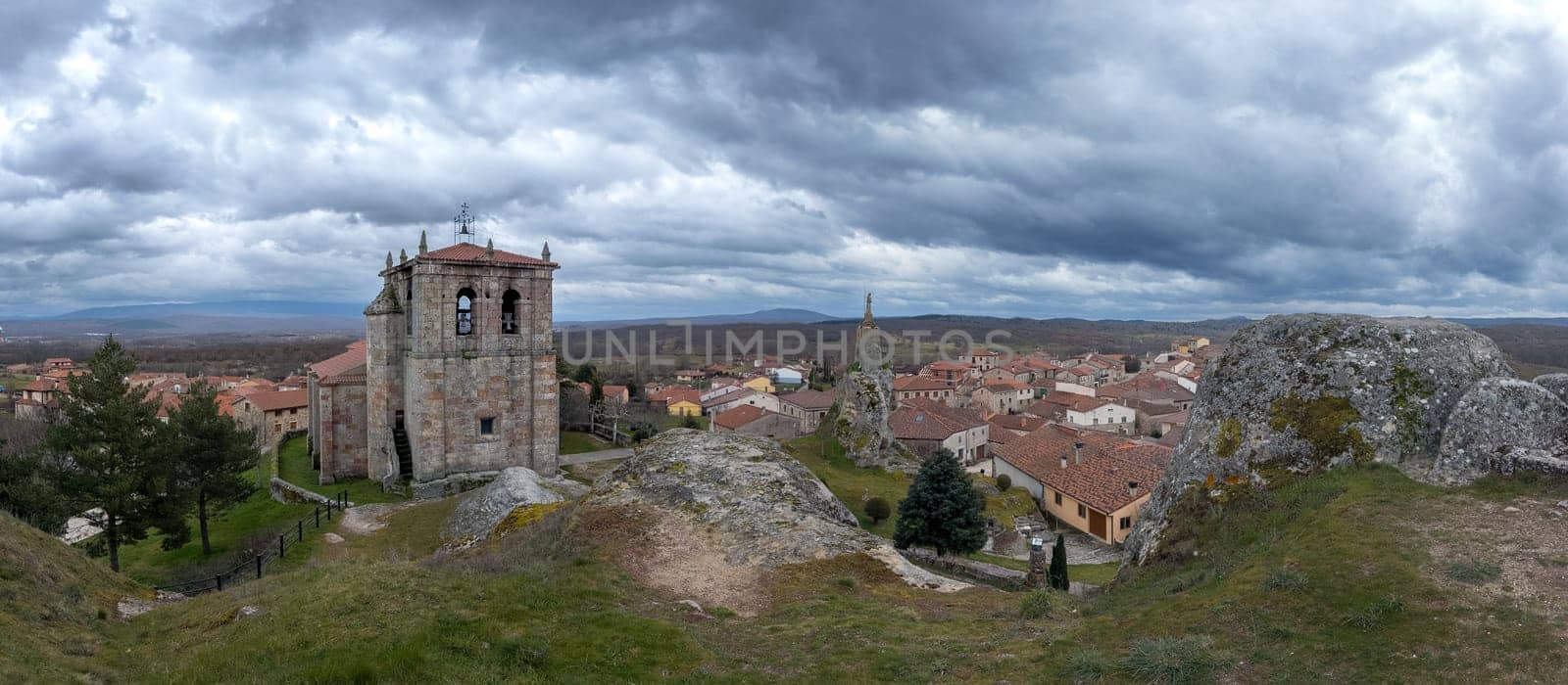 A charming village with a historic stone church is set beneath a dramatic cloudy sky.