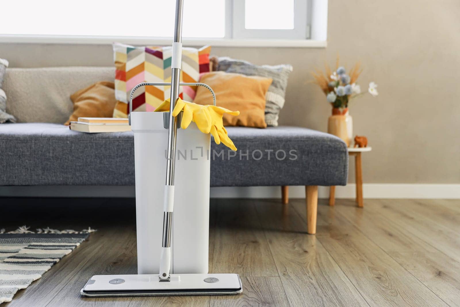 Cleaning supplies: mop, gloves, bucket with wringer sitting on wooden laminate floor in modern living room, wet equipment tools, housekeeping concept. Emphasizing home sanitation, cleanliness, hygiene