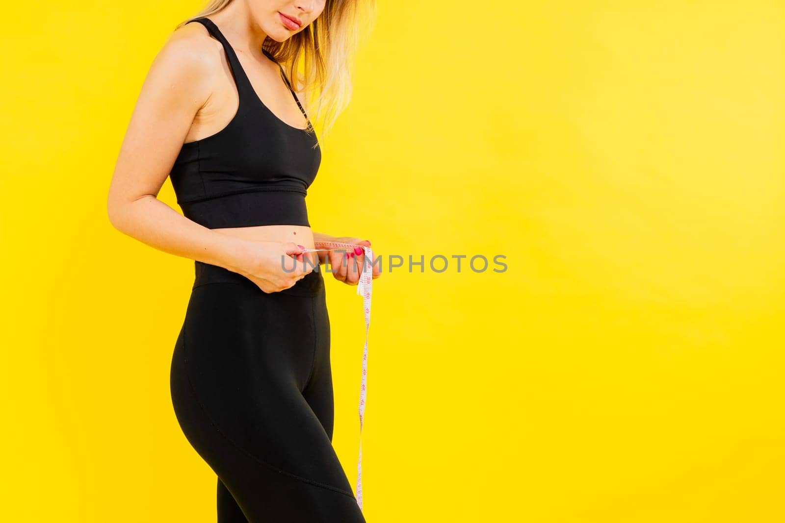 Smiling slim woman measuring her waist with tape. Fit young lady perfect shape, happy her body