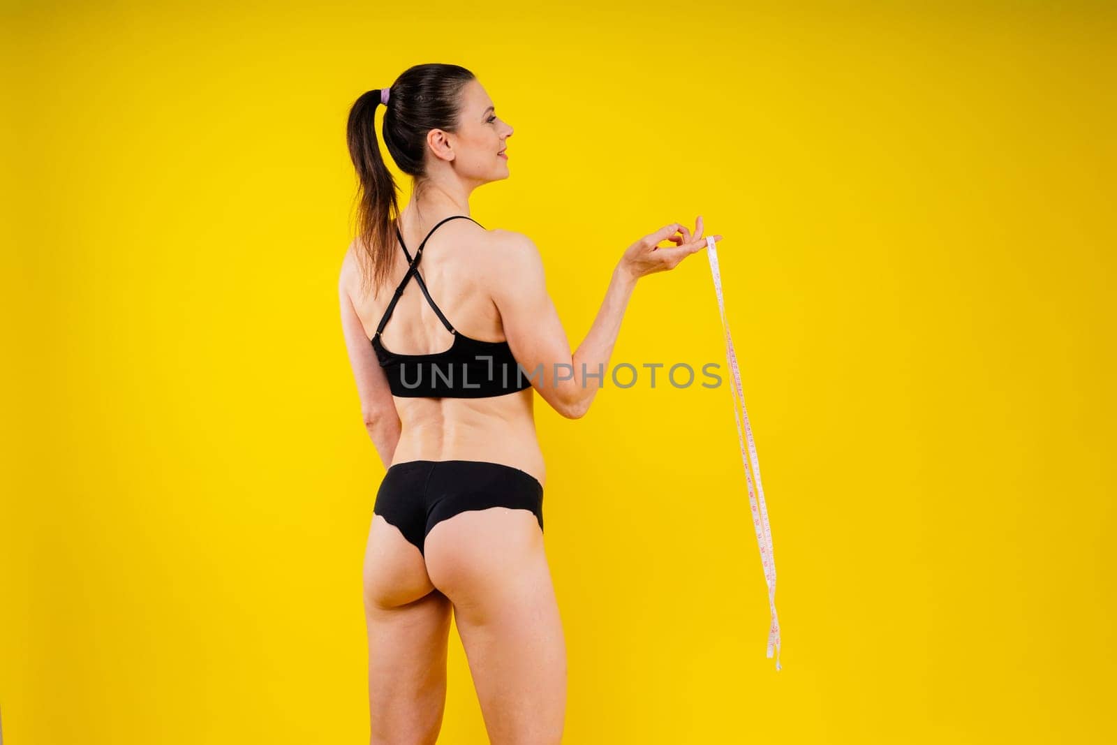 Smiling slim woman measuring her waist with tape. Fit young lady perfect shape, happy her body