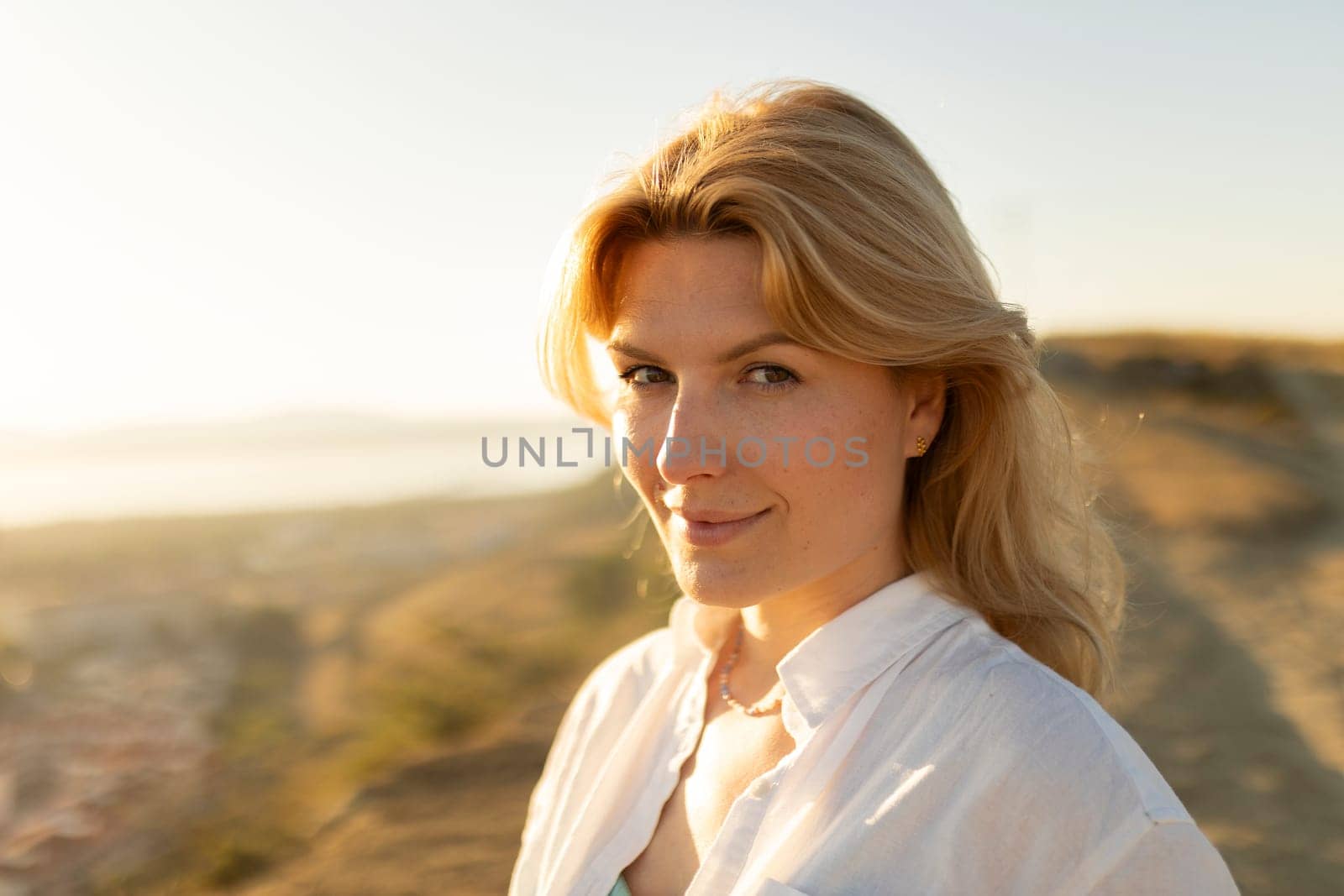 Portrait of a smiling blonde woman enjoying the golden hour sunlight on a hill