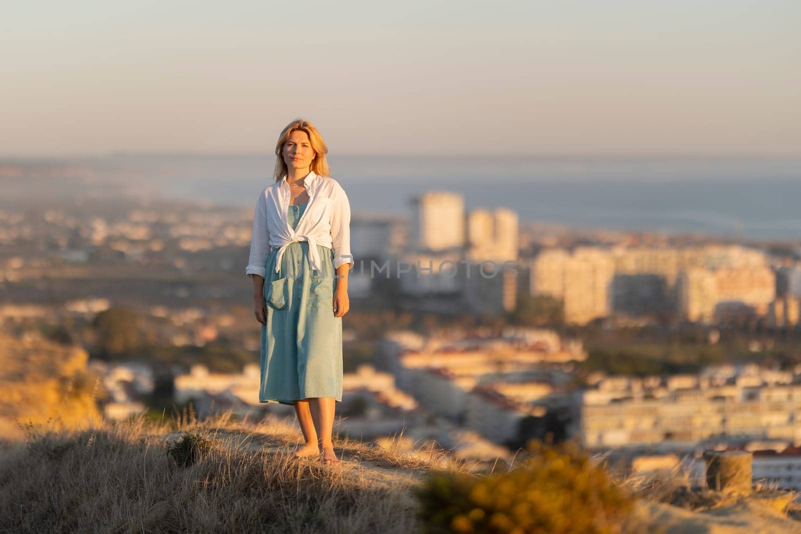 Woman in casual summer dress enjoying a beautiful sunset over a coastal city