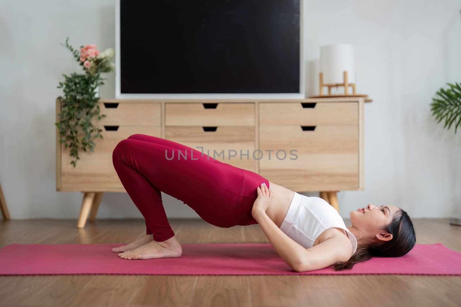 This image shows a woman doing the bridge pose, which strengthens core muscles and enhances flexibility in a comfortable home setting.