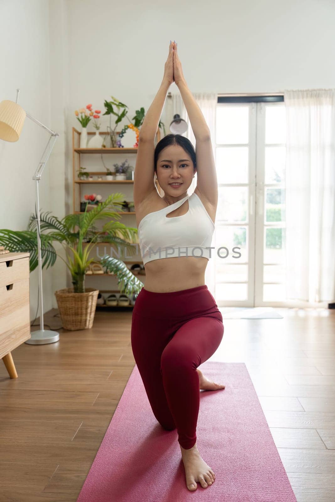 This image captures a woman in a yoga pose with arms extended upward, highlighting her commitment to mindfulness and physical fitness in a peaceful setting.