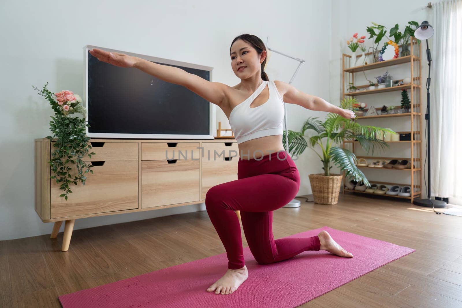 In this image, a woman gracefully performs a yoga lunge, exercising her balance and strength in a bright and inviting indoor space.
