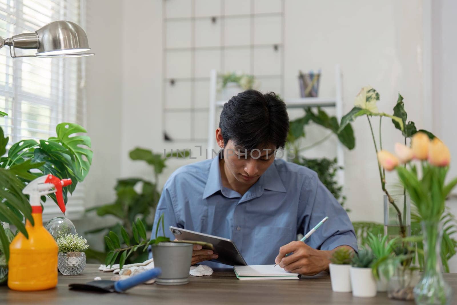 A young man takes notes on his gardening journey, meticulously planning how to care for his indoor plants with a notebook by his side.