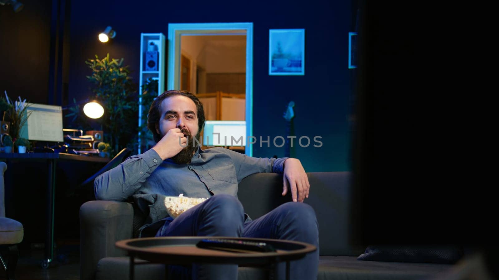 Joyous homeowner using TV to watch comedy films on streaming services, laughing at funny jokes. Radiant man in home theater consuming entertainment, amused by humorous movie scene, camera B
