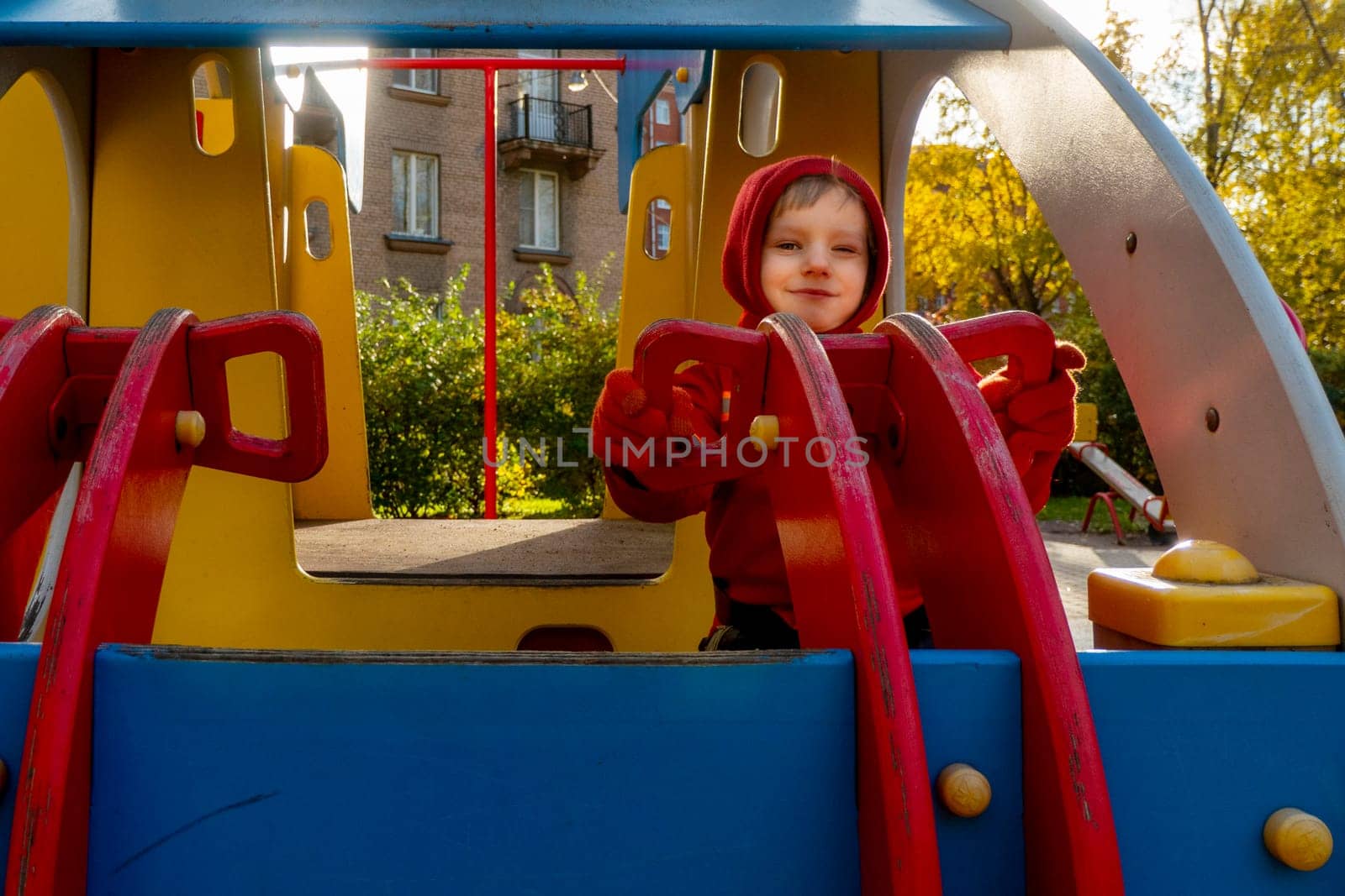 Child with red raincoat of firefighter clings to a rope in a playground during rain. High quality photo