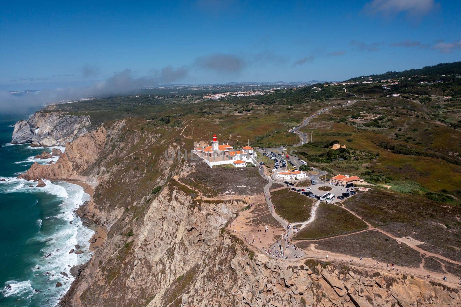 Aerial drone shot of Cabo da Roca Lighthouse and monument, showcasing cliffs, ocean views, and tourists visiting this popular landmark in Portugal