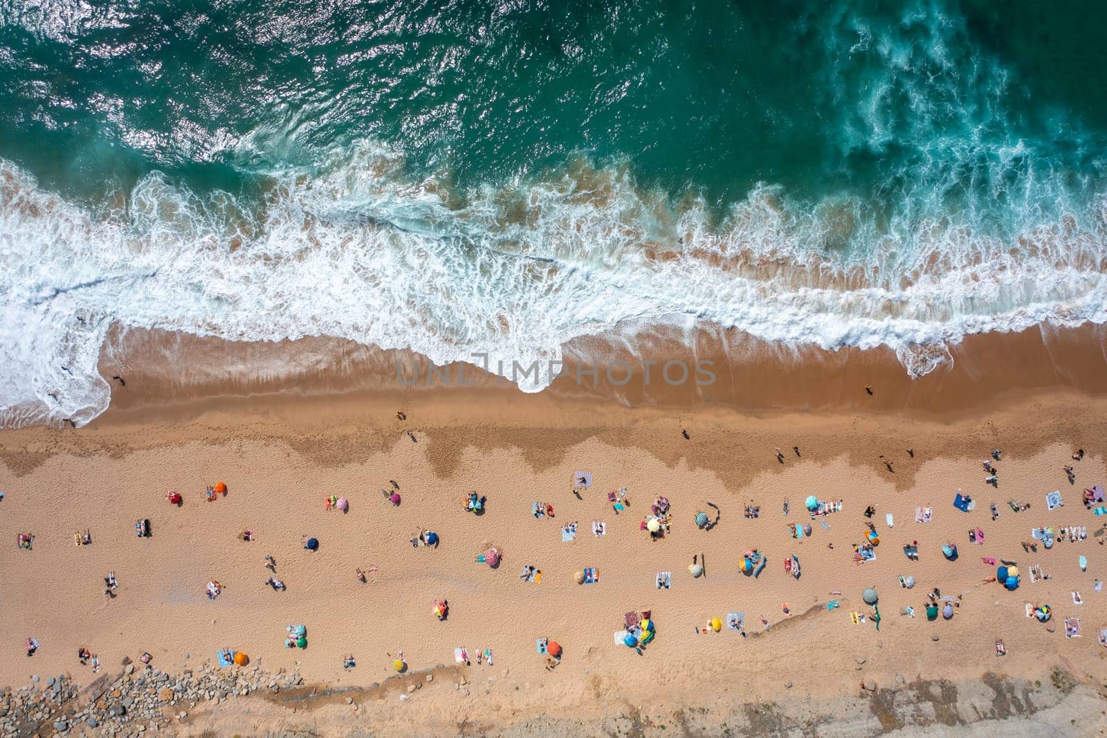 Overhead drone shot of tourists and parasols on sandy beach. A top-down view of people enjoying summer vacations by the sea on a sunny day