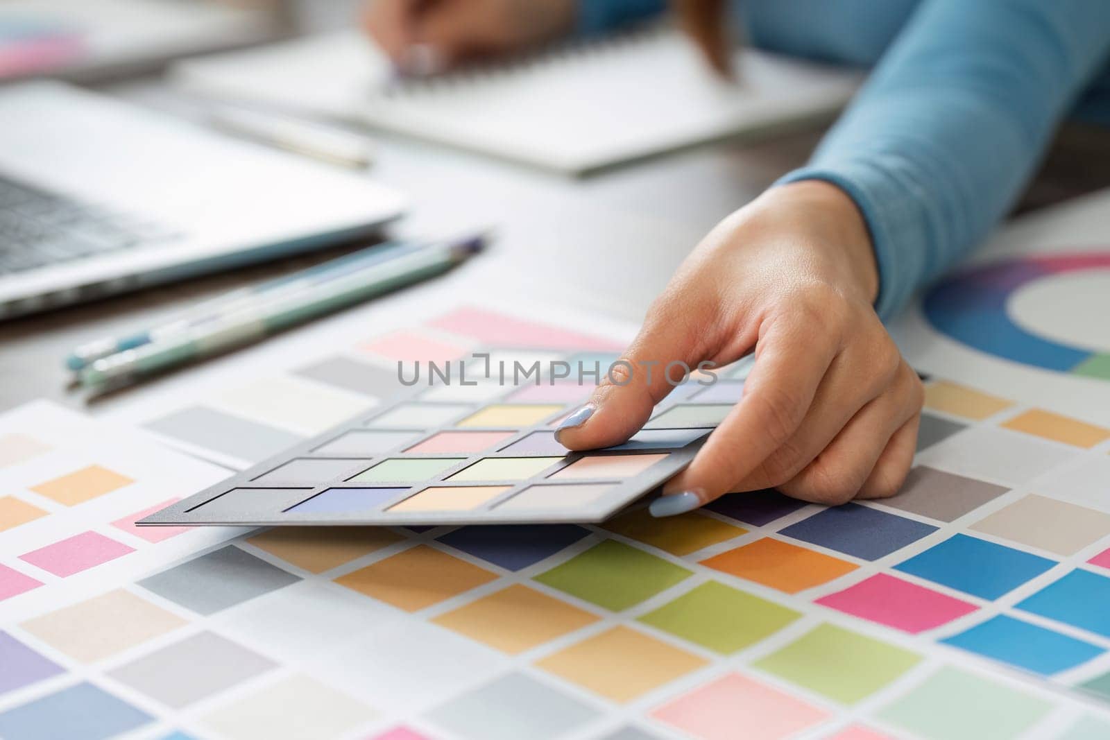 In a dynamic workspace, a designer is engaged in selecting colors from a physical palette while using a laptop.