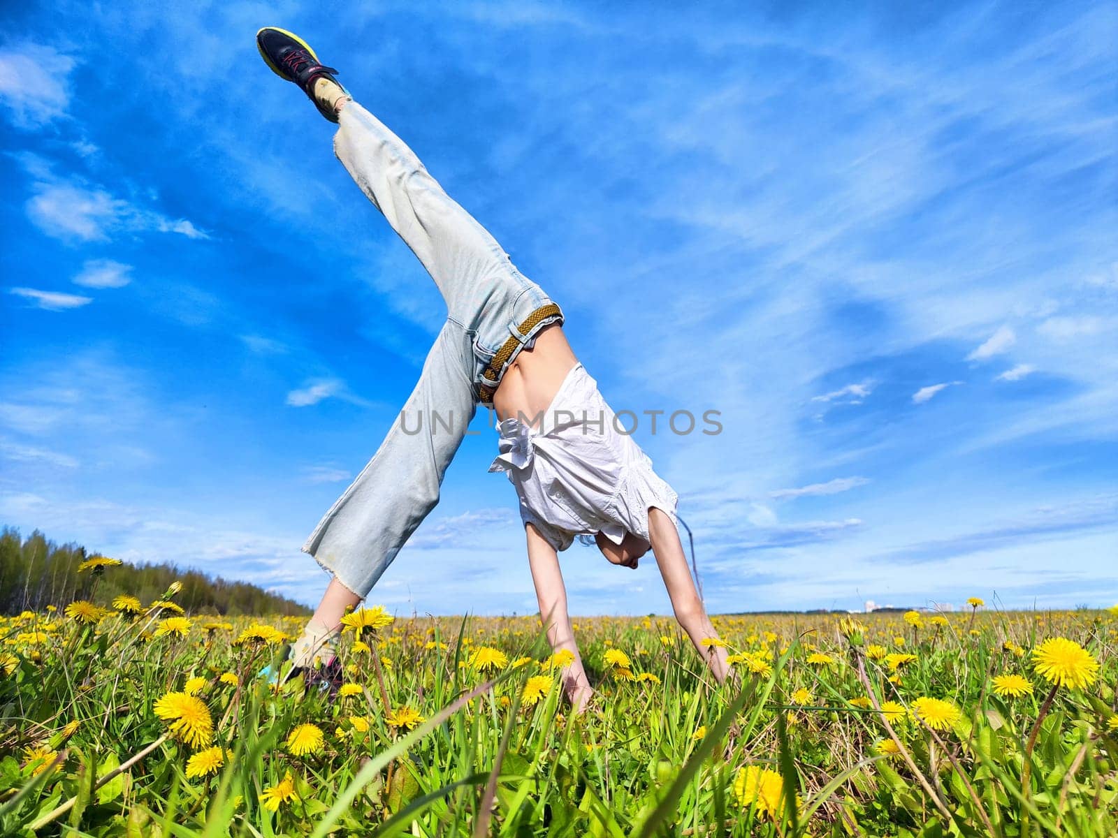 A joyful individual balances in a handstand on a colorful dandelion-filled meadow on a gorgeous and sunny day.