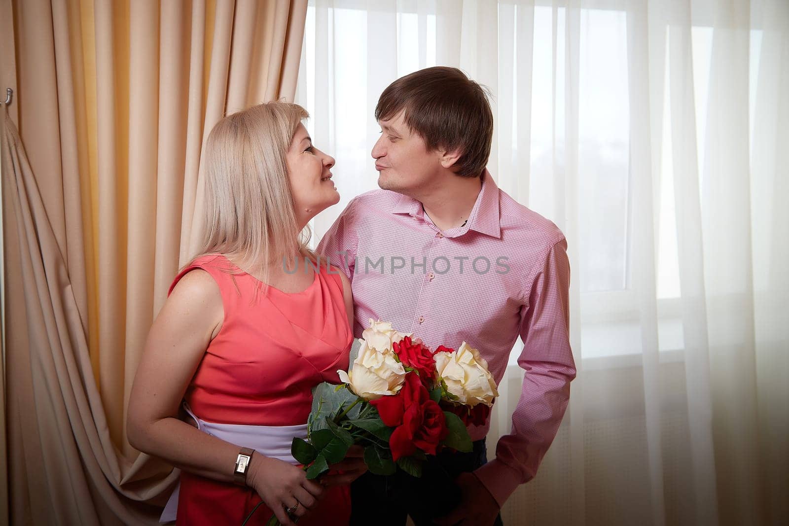 Couple joyfully poses together in a hotel room, holding flowers and celebrating their love during a romantic occasion.