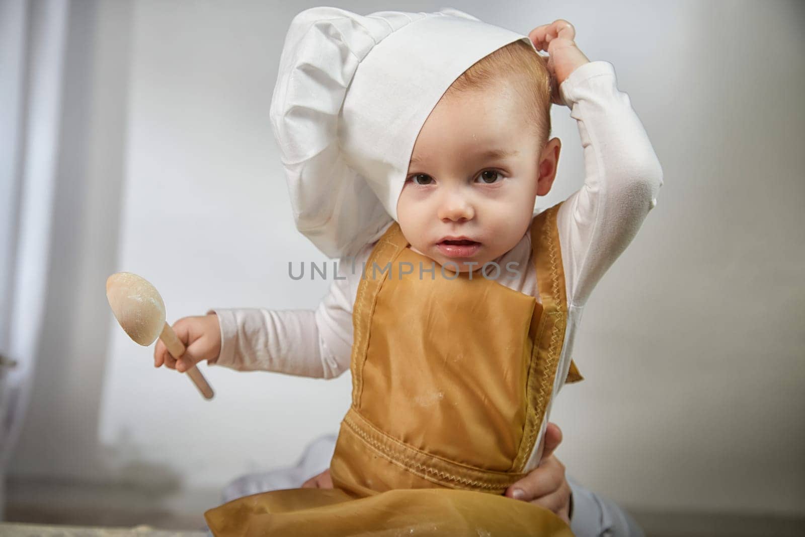 A curious boy wearing a chef's hat gazes thoughtfully while her photo is taken in a warm and inviting studio space.