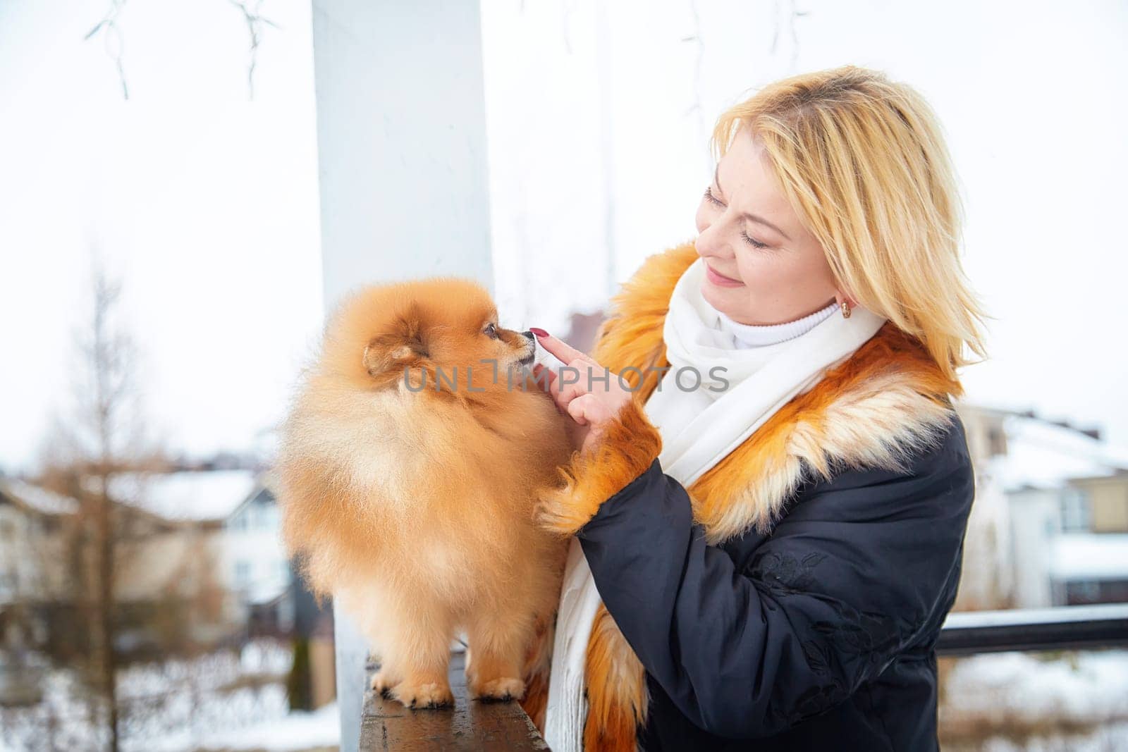 A middle-aged woman lovingly interacts with her fluffy pomeranian dog during a cold winter day.