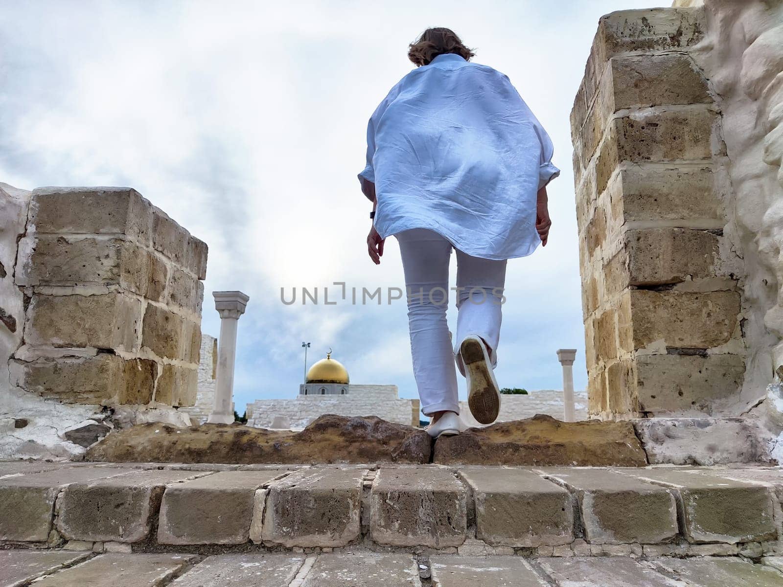 A middle-aged blonde woman walks up steps at a historic site, capturing the moment in a selfie while enjoying her travel excursion.