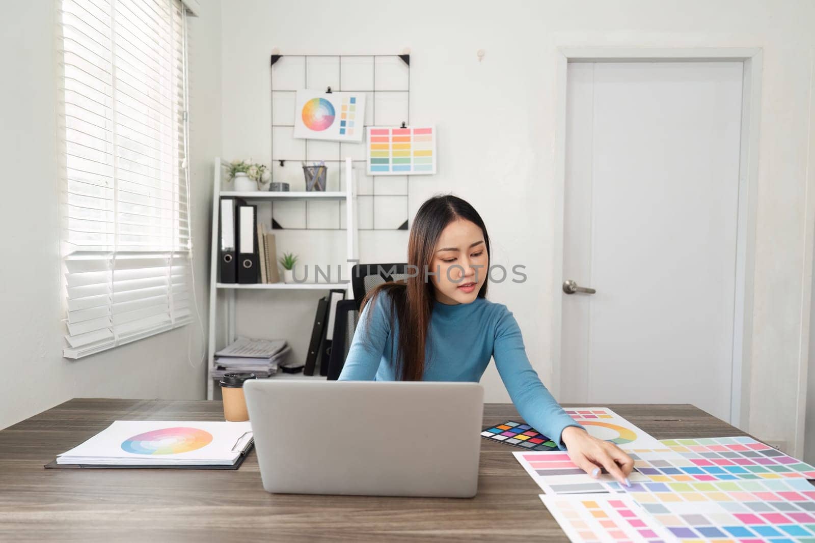 The designer engages with various color selections, creating a harmonious balance between digital tasks and hands-on color exploration in a professional setting.