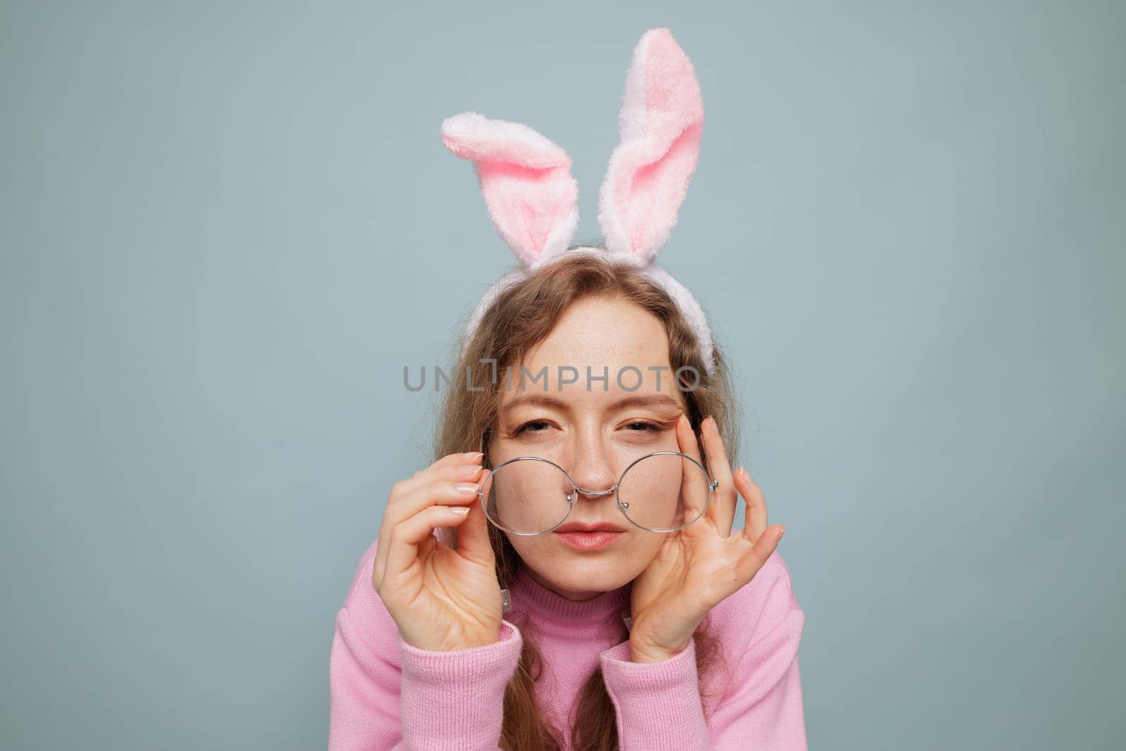 Portrait of a beautiful young woman with glasses, looking at you with curiosity, squinting, trying to get a closer look. Girl with poor eyesight in a pink sweater
