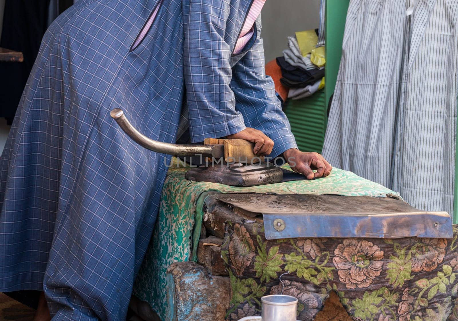 A tailor skillfully uses a foot-operated iron to smooth material in Esna, Egypt, showcasing traditional tailoring techniques