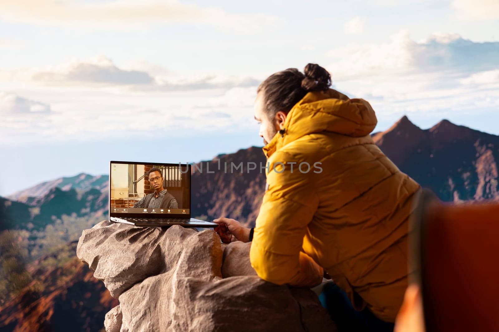 Young CEO entering a video call from the mountain top with a strong signal, always connected and discussing with associates about business matters. Workaholic businessman hiking.