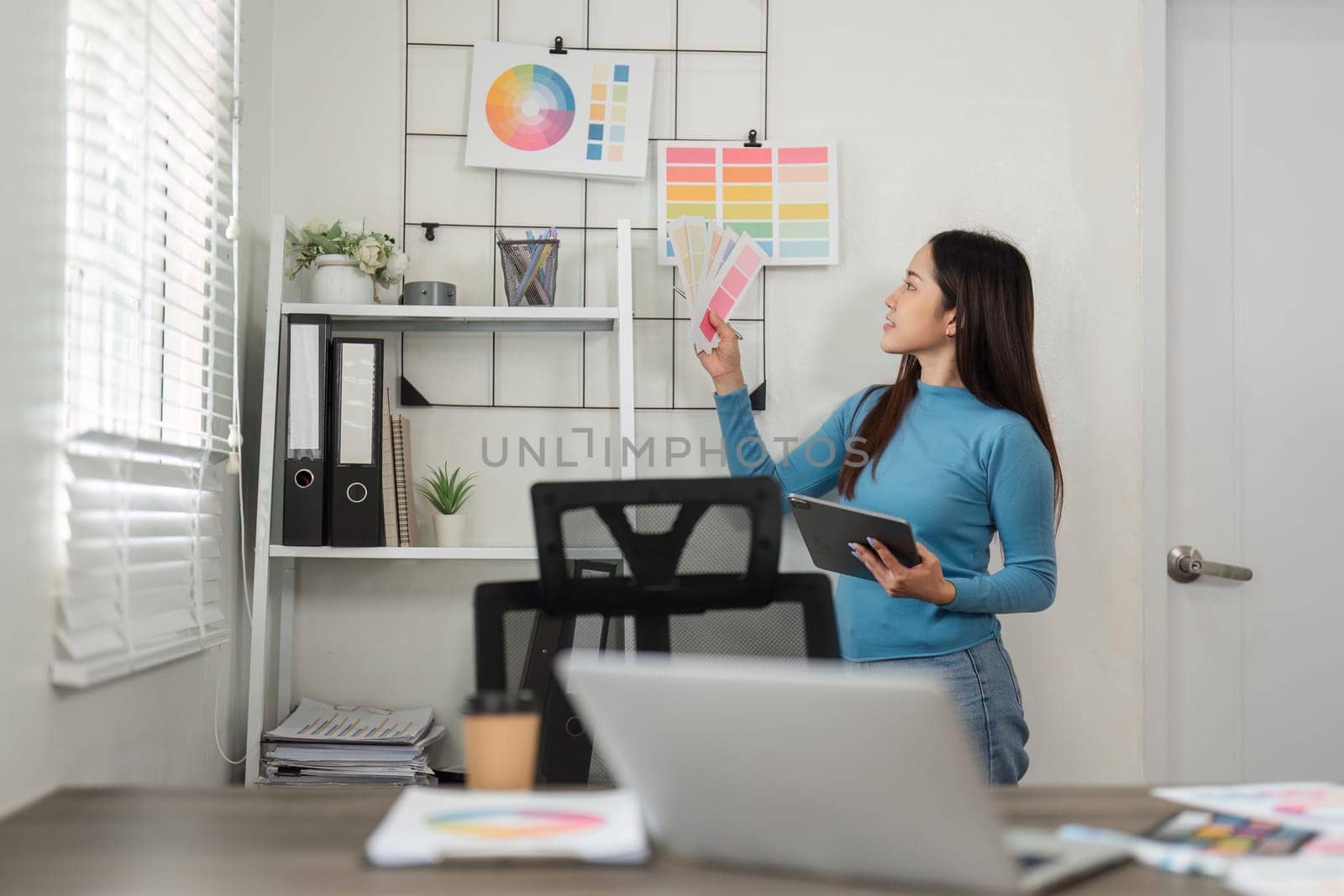 In the midst of a design process, a woman evaluates color swatches, contemplating the combination of hues for her project in a bright workspace.