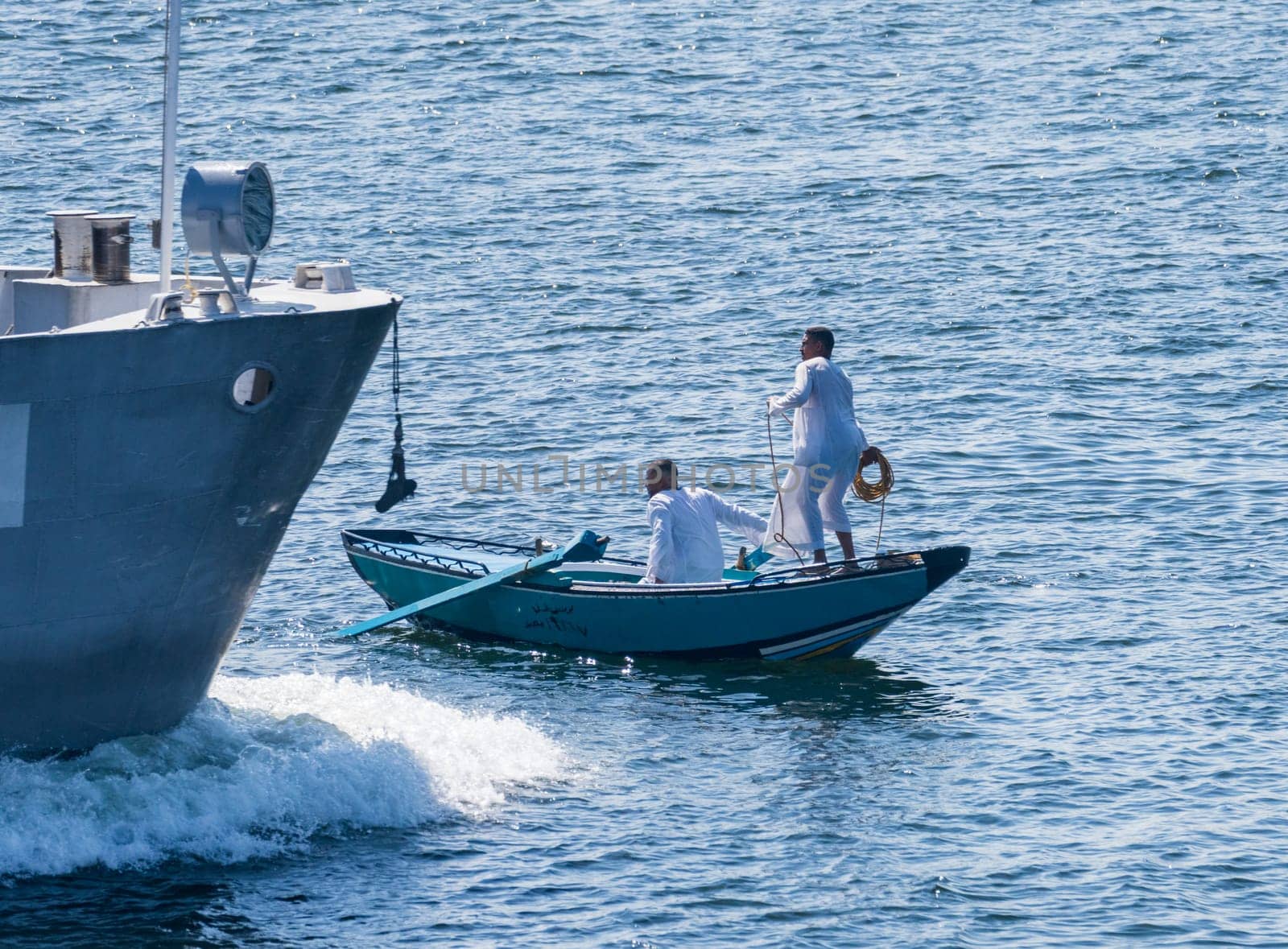 Esna, Egypt - 3 November 2024: Street vendor in a small rowboat selling textiles throwing rope to attach to a passing cruise ship.