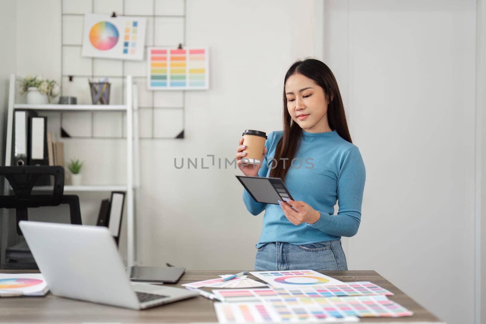 A thoughtful designer reviews design samples on her tablet, blending digital insights with her coffee break in a creative environment.