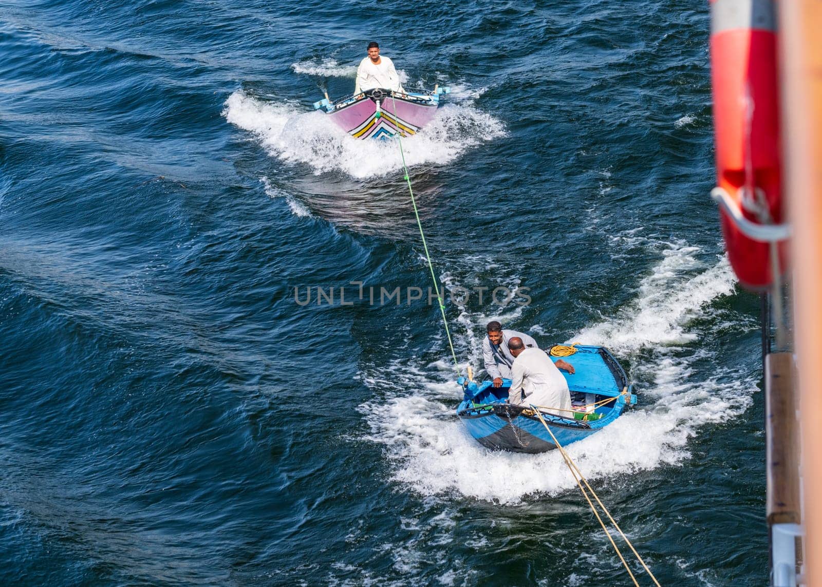 Esna, Egypt - 3 November 2024: Street vendors in two small rowboats selling textiles while attached and being towed by a cruise ship.