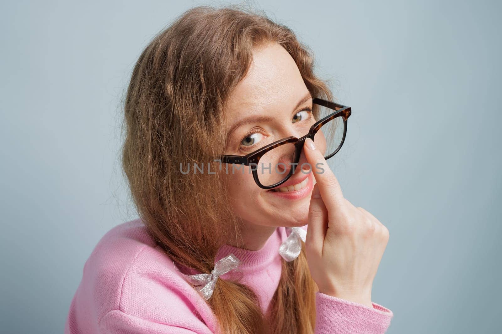 A woman with long hair and glasses playfully adjusts her glasses, smiling at the camera. She is wearing a pink sweater, concept vision problem