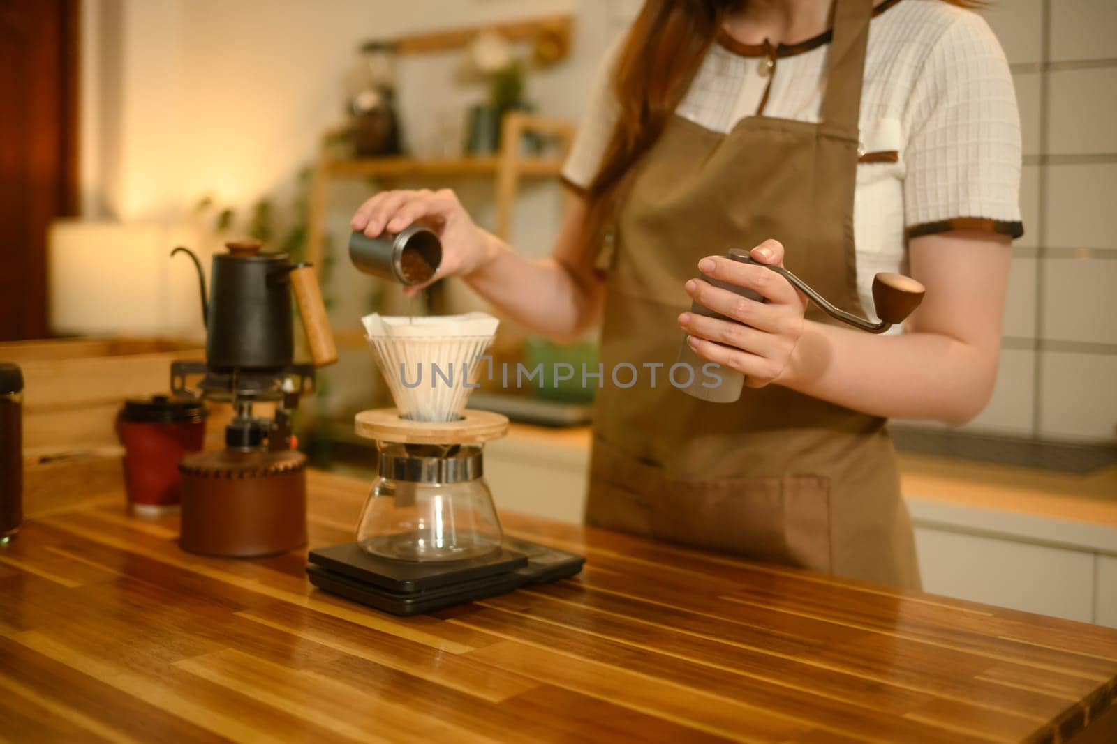 Young woman pouring ground coffee into dripper while making a fresh brew in a kitchen.